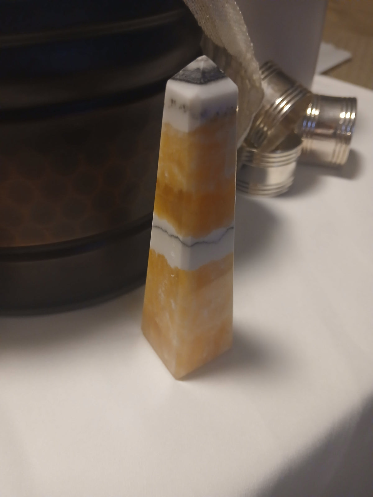 Polished Golden Calcite obelisk with white banding and pointed top standing on a white surface.