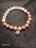 Pink and peach stone bead bracelet with silver heart charm on dark fabric.
