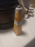 Polished Golden Calcite obelisk with white banding and pointed top standing on a white surface.